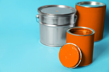 Cans and bucket of orange paint on turquoise background. Space for text