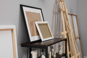 Wooden easel near shelving unit with canvases and small sculptures in artist's studio