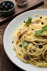 Delicious pasta with anchovies, olives and basil on wooden table, closeup