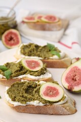 Tasty bruschettas with cream cheese, pesto sauce, figs and fresh basil on plate, closeup