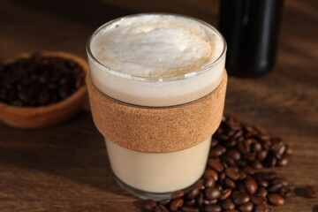 Bottle of delicious syrup, glass of coffee and beans on wooden table, closeup