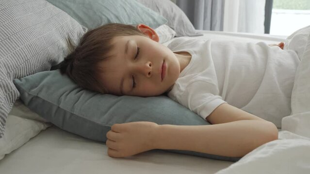 Portrait of little boy sleeping in bed at morning. Modern bedroom with big window