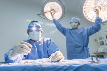 Doctor or surgeon in blue gown holding surgical lamp to adjust light inside operating theatre with...