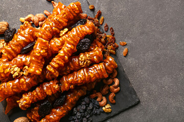 Board with tasty churchkhela, nuts and dried fruits on dark background