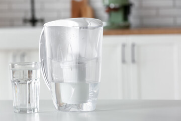 Modern filter jug and glass of water on table in kitchen