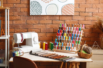 Fabric samples with thread spools and sewing machine on table in atelier