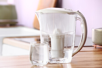 Modern filter jug and glass of water on kitchen counter, closeup
