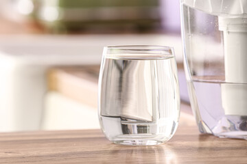 Glass of pure water and filter jug on kitchen counter, closeup