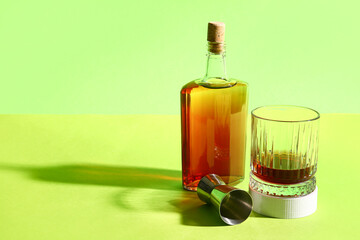 Bottle of rum, glass and measure cup on green background