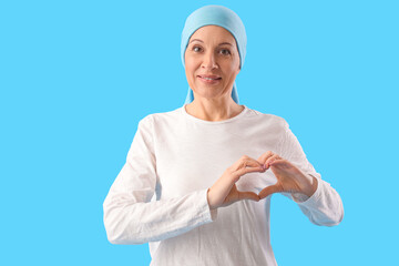 Mature woman after chemotherapy making heart with her hands on blue background