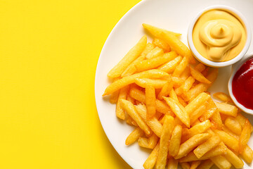 Plate with tasty french fries and sauces on yellow background, closeup