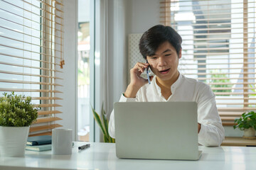 Handsome asian marketing sales consulting client making offer selling talking on phone at working desk.