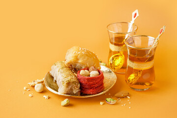 Plate with tasty baklava and glasses of Turkish tea on orange background