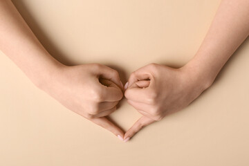 Woman making heart with her hands on beige background
