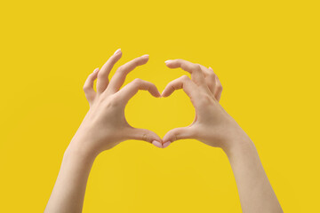 Woman making heart with her hands on yellow background