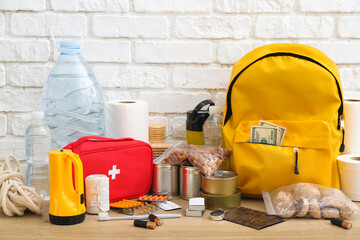 Necessities for emergency bag on wooden table near white brick wall