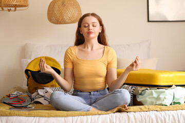 Young woman meditating while packing her things for travelling in bedroom