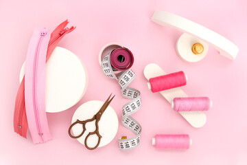 Podiums with scissors, thread spools, measuring tapes and zips on pink background