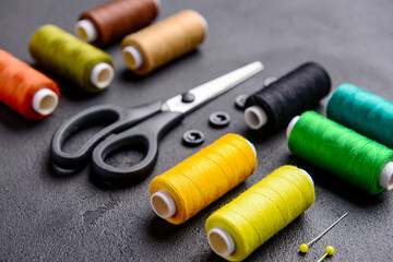 Composition with different thread spools and sewing supplies on dark background, closeup