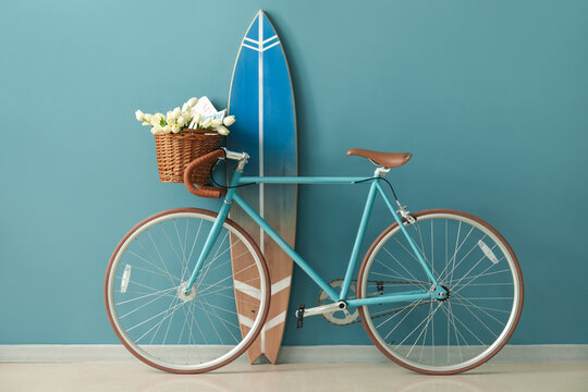 Bicycle with flowers and surfboard near blue wall in room