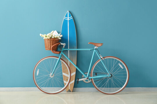 Bicycle with flowers and surfboard near blue wall in room