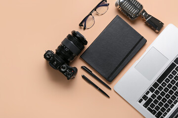Notebook with microphone, laptop, photo camera and eyeglasses on beige background