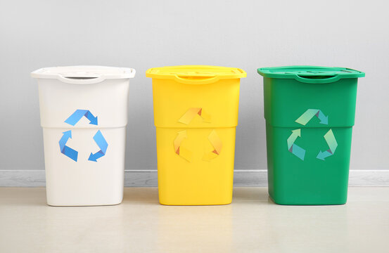 Different garbage bins with recycling symbol near white wall