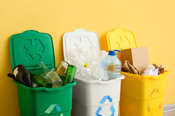 Trash bins with recycling symbol and different garbage near yellow wall