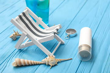Fototapeta na wymiar Composition with miniature deck chair, bottle of sunscreen and compass blue wooden background