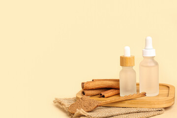 Fototapeta na wymiar Board with bottles of essential oil, cinnamon sticks and powder on beige background
