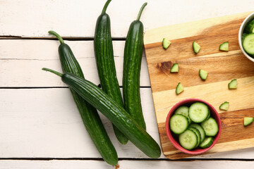 Fresh cucumbers and cut pieces on light wooden background, closeup