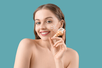 Beautiful naked young woman with sunscreen cream on her face and sea shell against blue background