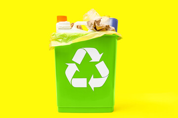 Trash bin with different garbage on yellow background