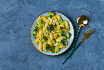 Plate with tasty pasta and broccoli on blue background