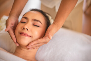 Beautiful asian woman in close up shot being massaged with smile on her face by professional masseuse hands on white bed.