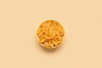 Bowl with raw conchiglie pasta on yellow background