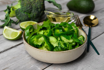 Bowl of salad with green vegetables on grey wooden background