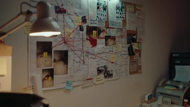 Detective office with no people during night time, murder investigation materials connected by red string on pinboard on the wall. CSI work concept