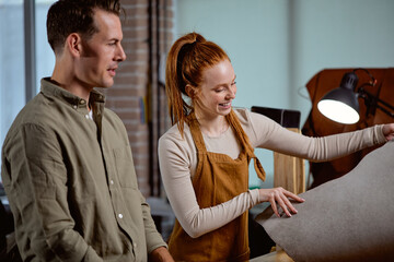 smiling happy ginger girl holding cloth of leather shsowing it to her co-worker, colleague, close up side view shot.business success.happiness