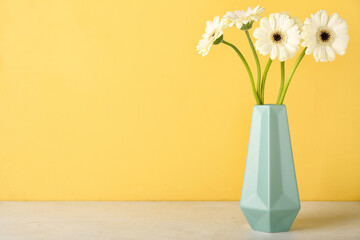 Vase with gerbera flowers on table near yellow wall