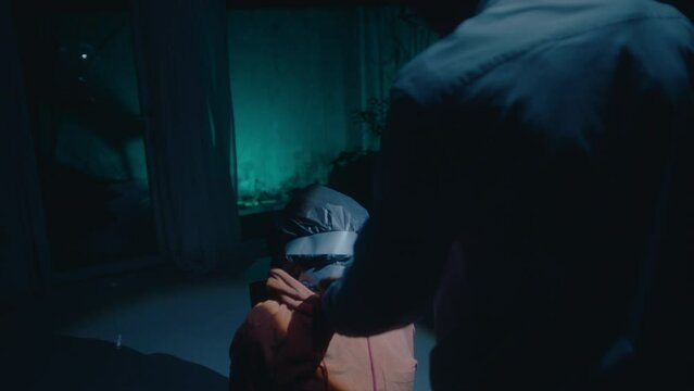 African American police officer walking with flashlight through dark house at night, finding dead body tied to chair with plastic bag on head, discovering crime scene of murder