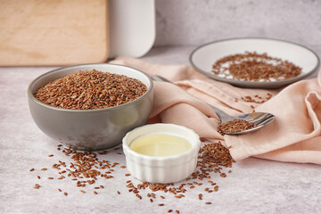 Bowl with flax oil and seeds on light background