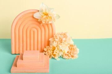 Decorative plaster podiums with flowers on turquoise table against yellow background