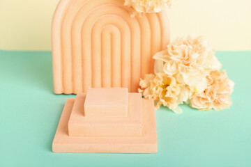 Decorative plaster podiums with flowers on turquoise table against yellow background