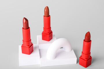 Decorative plaster podiums and lipsticks on grey background