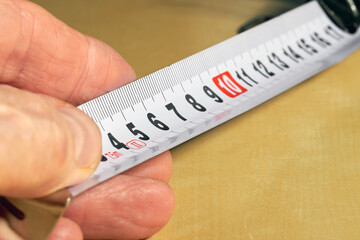 fingers hold the tip of a tape measure, close-up, copy space