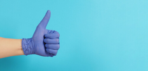 The hand is wearing a violet or purple latex glove and do like hand sign on blue background.