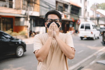 Fototapeta premium Asian young man wearing face mask to protect PM 2.5, protect pollution, anti smog and viruses on road in the city. Global warming concept. Healthcare concept. Environmental pollution concept.