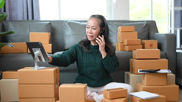 Senior Asian business owner woman prepare parcel box and standing check online orders for deliver to customer on tablet, laptop Shopping Online concept..