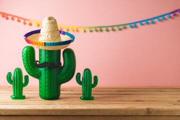 Mexican party concept with cactus and sombrero hat on wooden table over pink background. Cinco de...